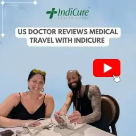A smiling American man and woman are seated at a table. The image promotes their review of medical travel with IndiCure.